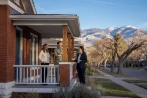 best real estate agents in denver - couple meeting a listing agent on the porch of a red brick Denver bungalow with the snow dusted Front Range foothills behind them